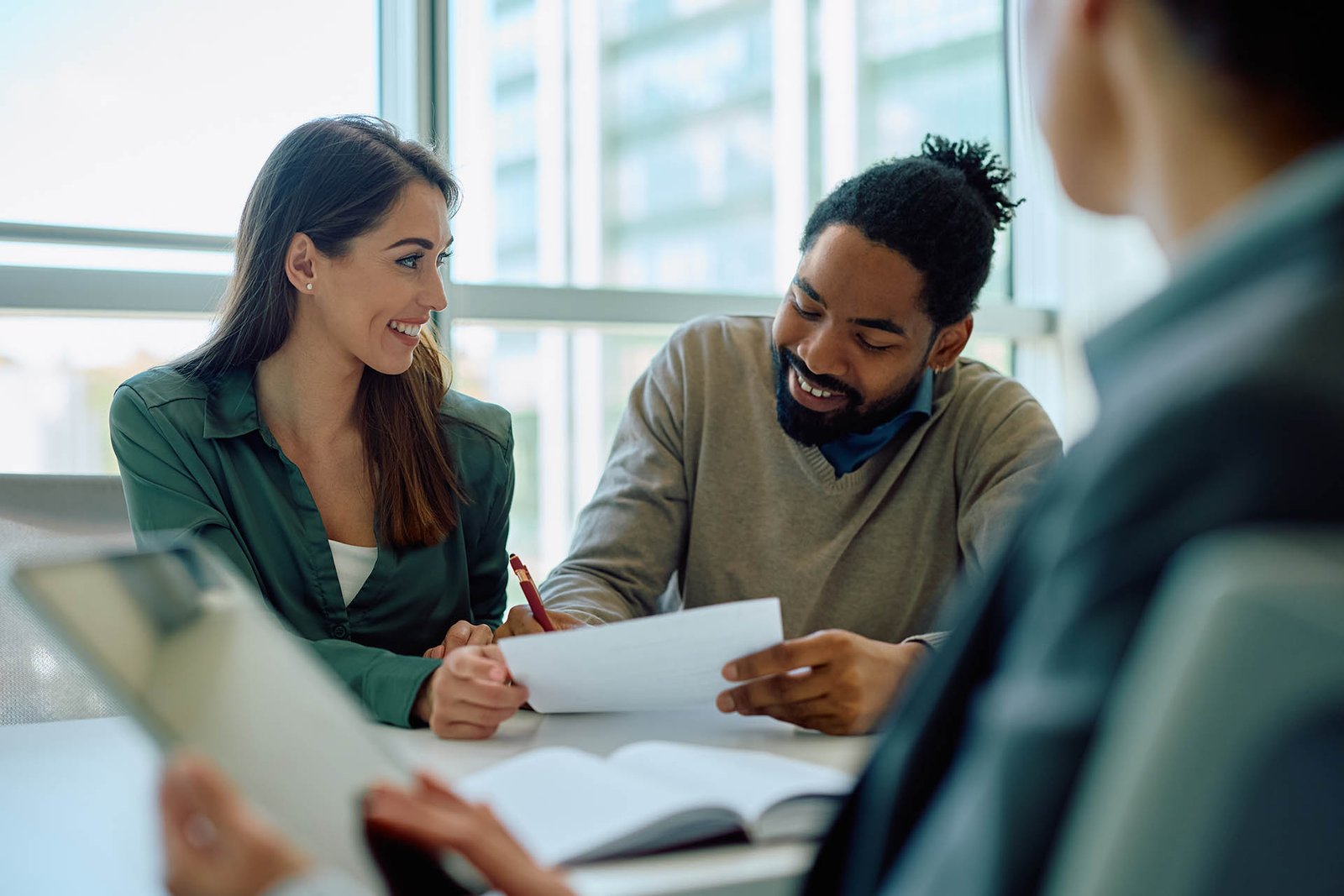 Happy African American man signing an agreement while being with his wife on a meeting with financial advisor in the office.